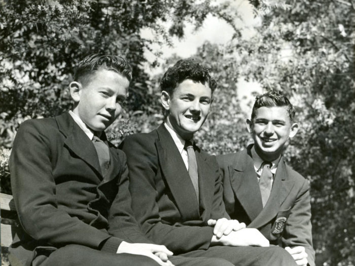 three boys sitting on bench with trees in background